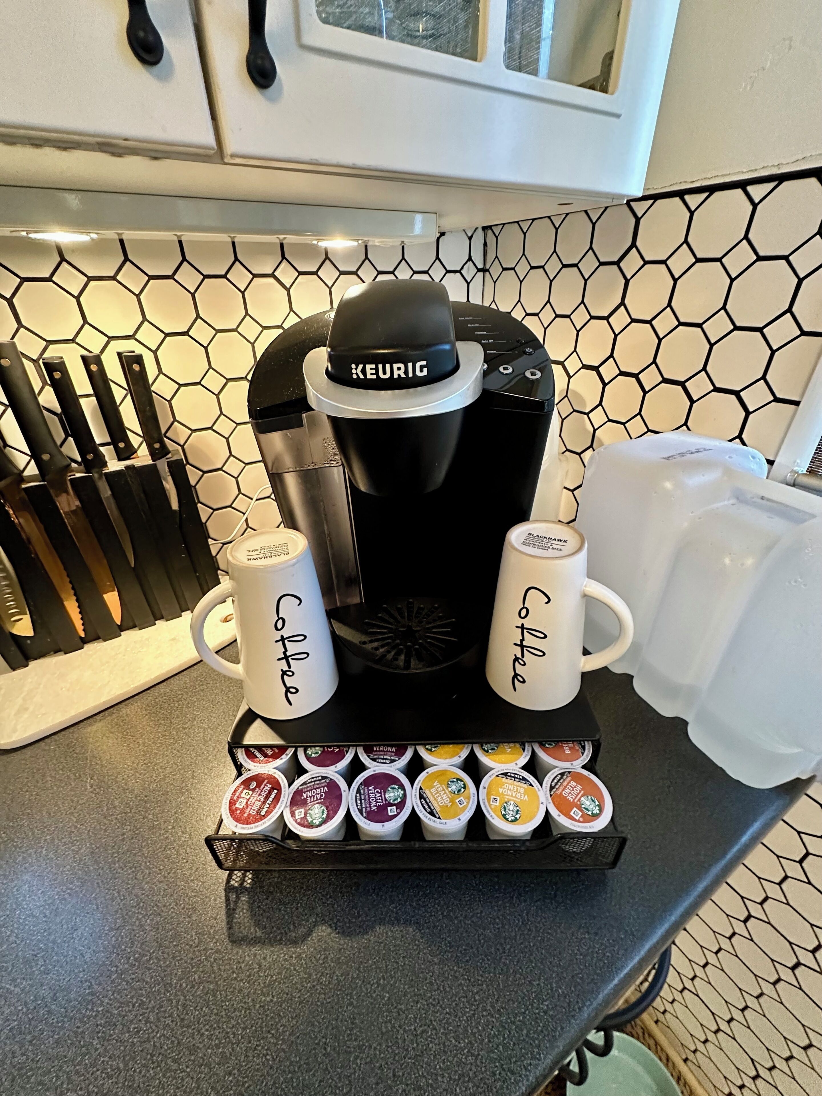 Une machine à café Keurig avec deux tasses à café posées sur un plateau contenant des dosettes de café.