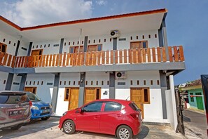 Un edificio de dos pisos con balcón, varias puertas y automóviles estacionados.