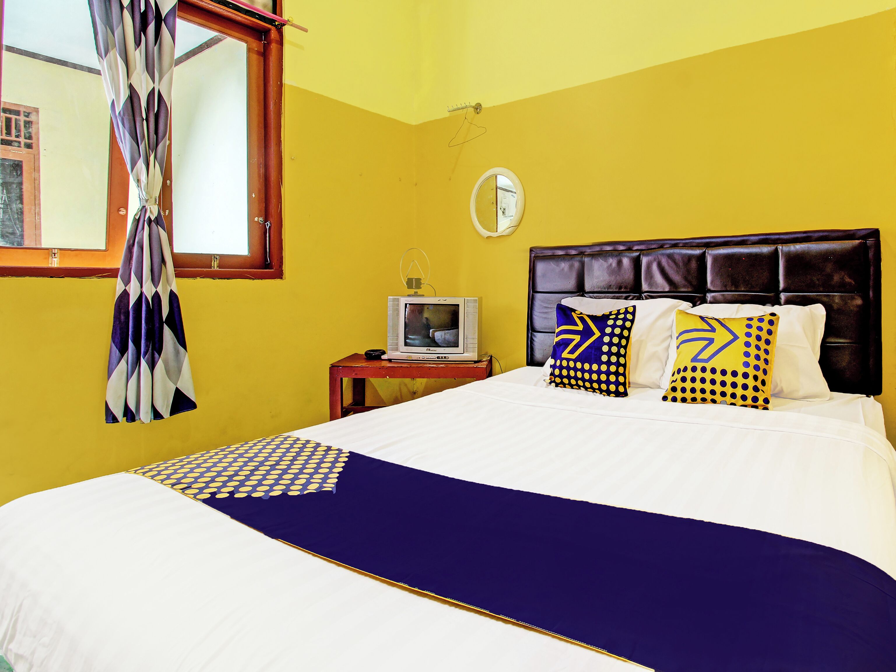 Una habitación con una cama, un televisor sobre una mesita de noche y una ventana con cortinas.