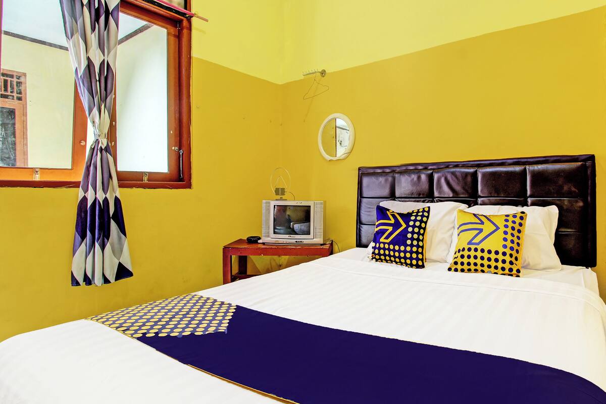 Una habitación con una cama, un televisor sobre una mesita de noche y una ventana con cortinas.
