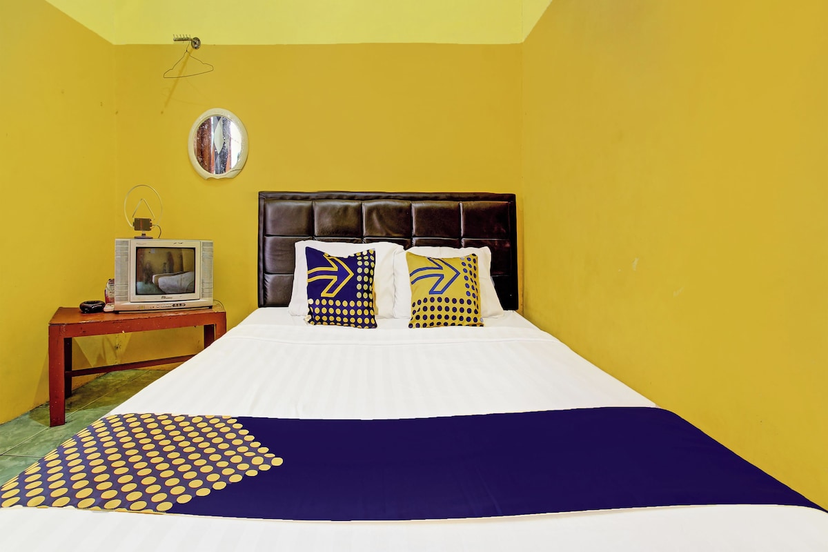 Una habitación de hotel con una cama, un televisor sobre una mesita auxiliar y un espejo en la pared.