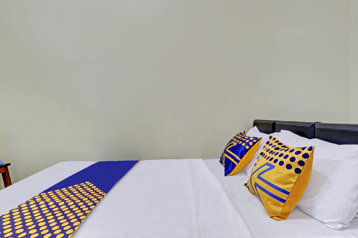 Una cama bien hecha con sábanas blancas, una colcha de color azul y amarillo, y dos almohadas decorativas con diseños azules y amarillos.