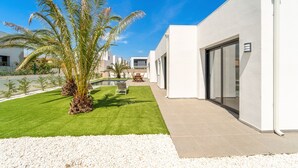 A modern building with a white exterior, a patio area with artificial grass, and a pool in the background. - WELCS VILLA 167 EMP con piscina privada (Empuriabrava)