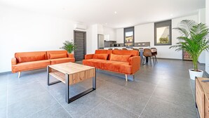 A spacious living area with a modern orange sofa set, a wooden coffee table, and a kitchen in the background. - WELCS VILLA 167 EMP con piscina privada (Empuriabrava)