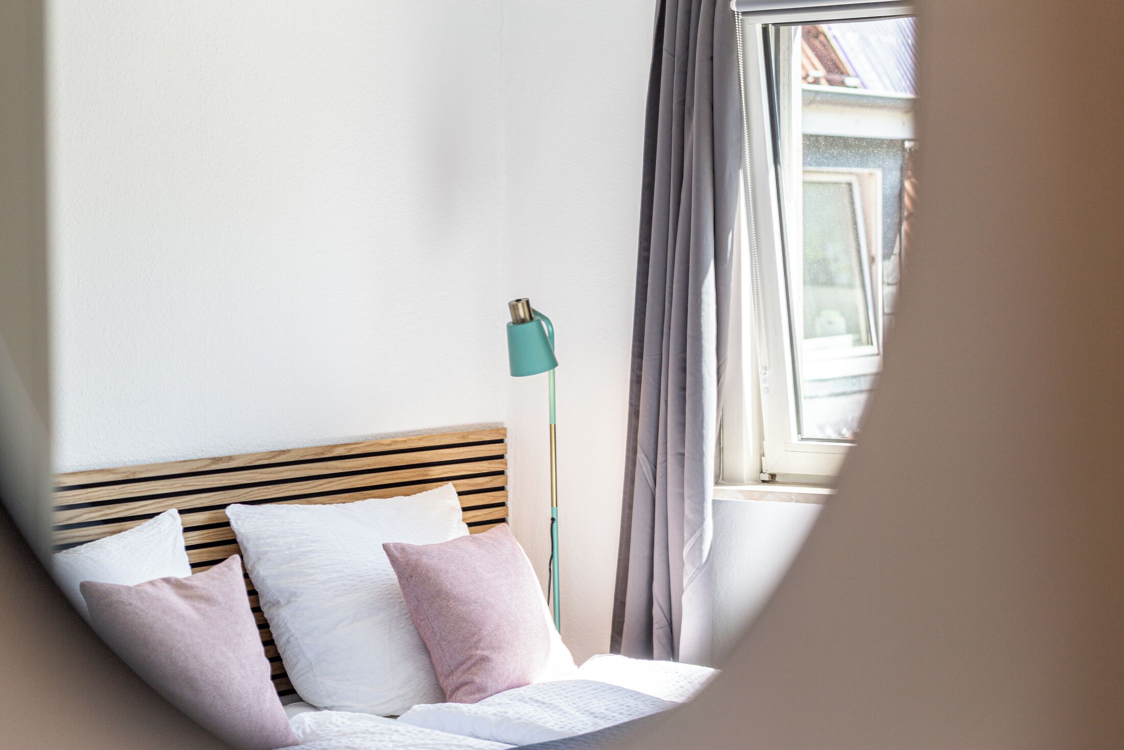 Ein ordentlich bezogenes Bett mit Kissen, einem Holzkopfstück und einer Stehlampe.
