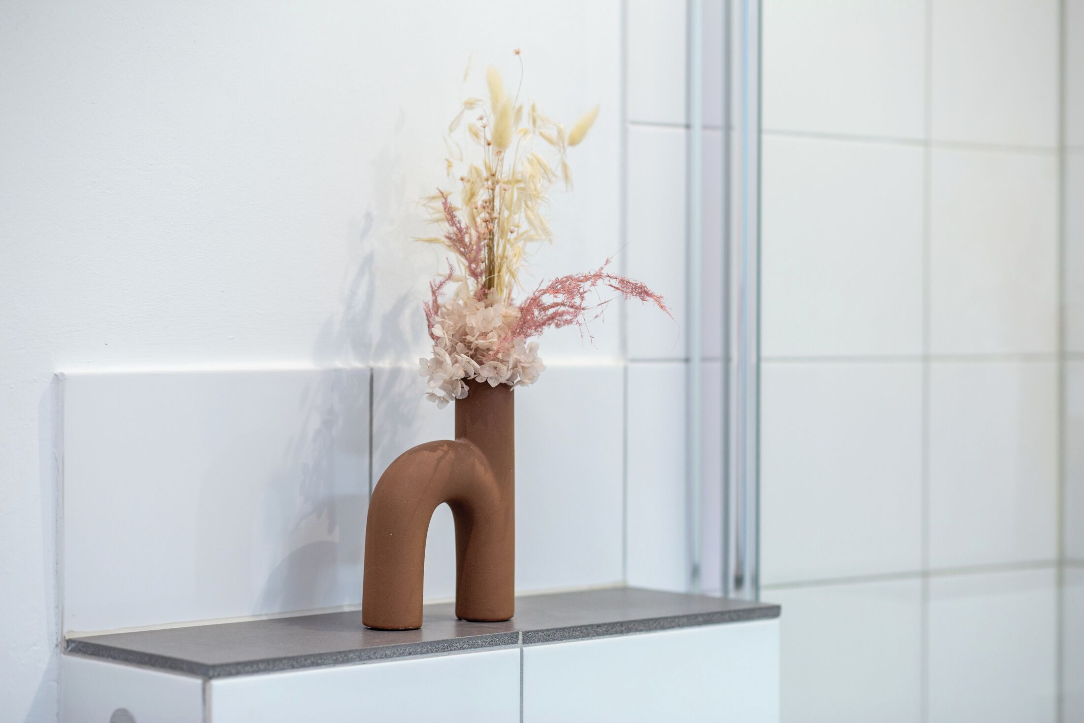 A vase with flowers on a white shelf against a white wall.