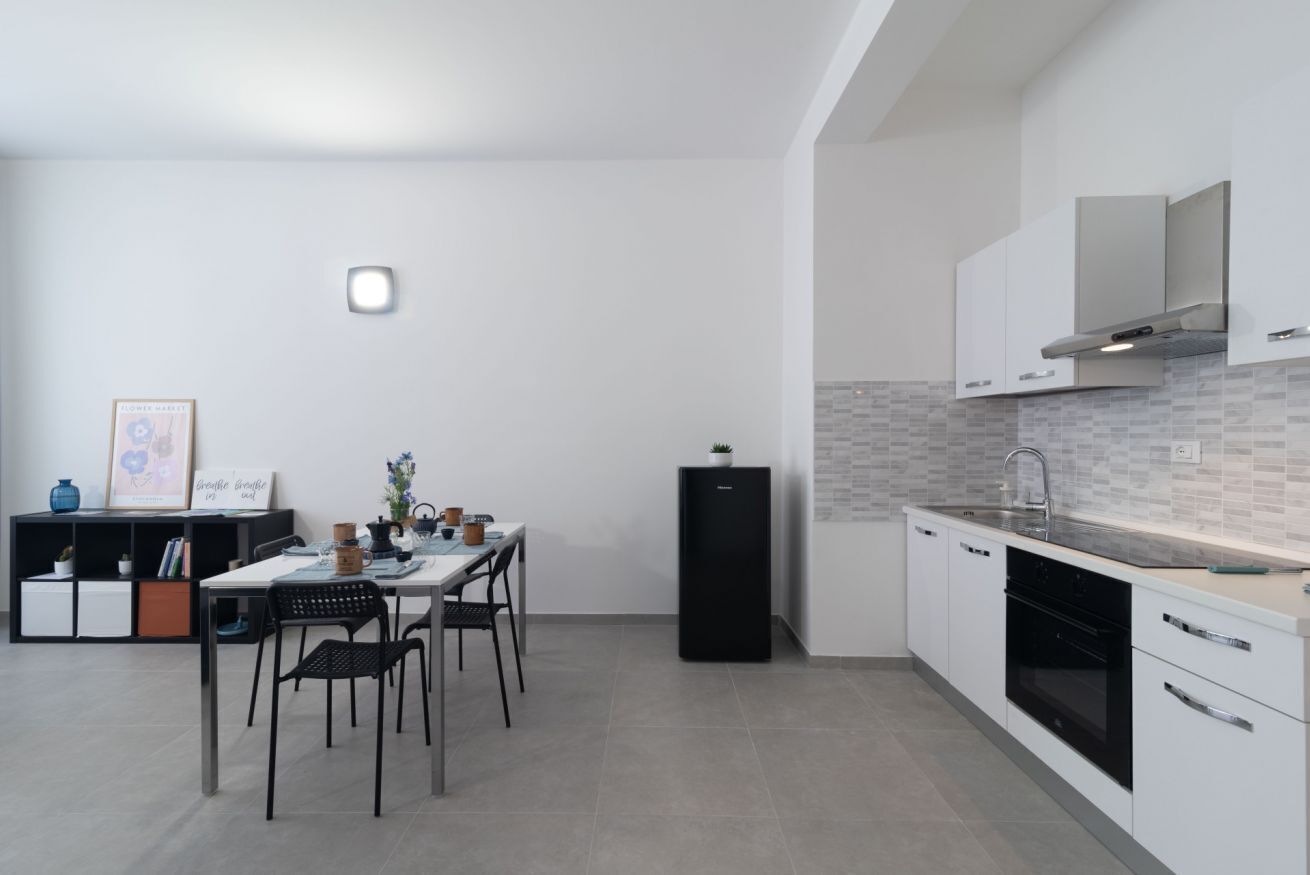 A modern kitchen with white cabinets, a black refrigerator, and a dining area with a table and chairs.