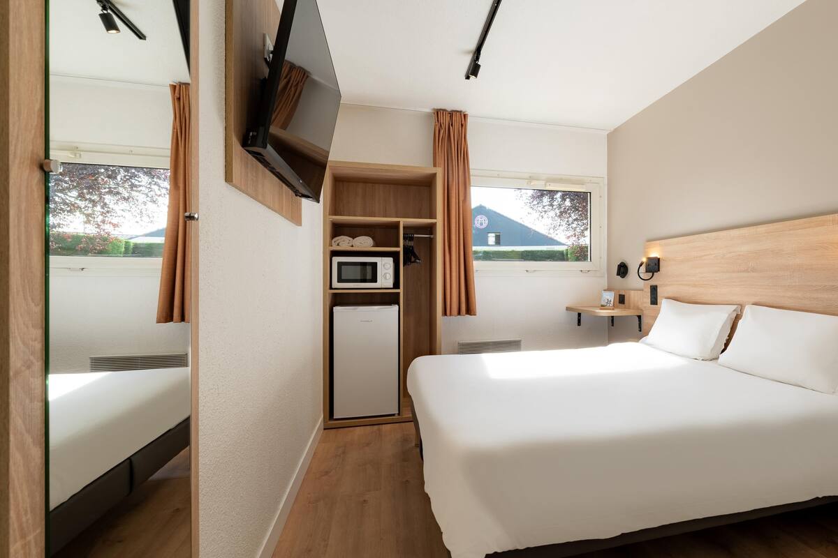 A bedroom with a bed, a TV mounted on the wall, a microwave, and a small kitchenette.