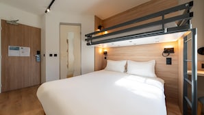 Una habitación de hotel moderna con cama, paneles de madera, una lámpara de pared y una puerta con un cartel.
