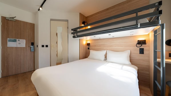 A modern hotel room with a bed, wooden paneling, a wall-mounted light, and a door with a sign. - Kyriad ECO Lille SUD - Noyelles-Godault (Noyelles-Godault)