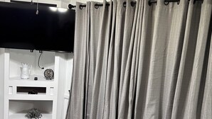 Habitació amb ventilador de sostre, televisió de pantalla plana i estant amb objectes decoratius.