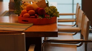 A dining table with a fruit bowl, a vase with red flowers, and a view of the sea through large windows. - Private Villa Siray Beach Front  (Ratsada)