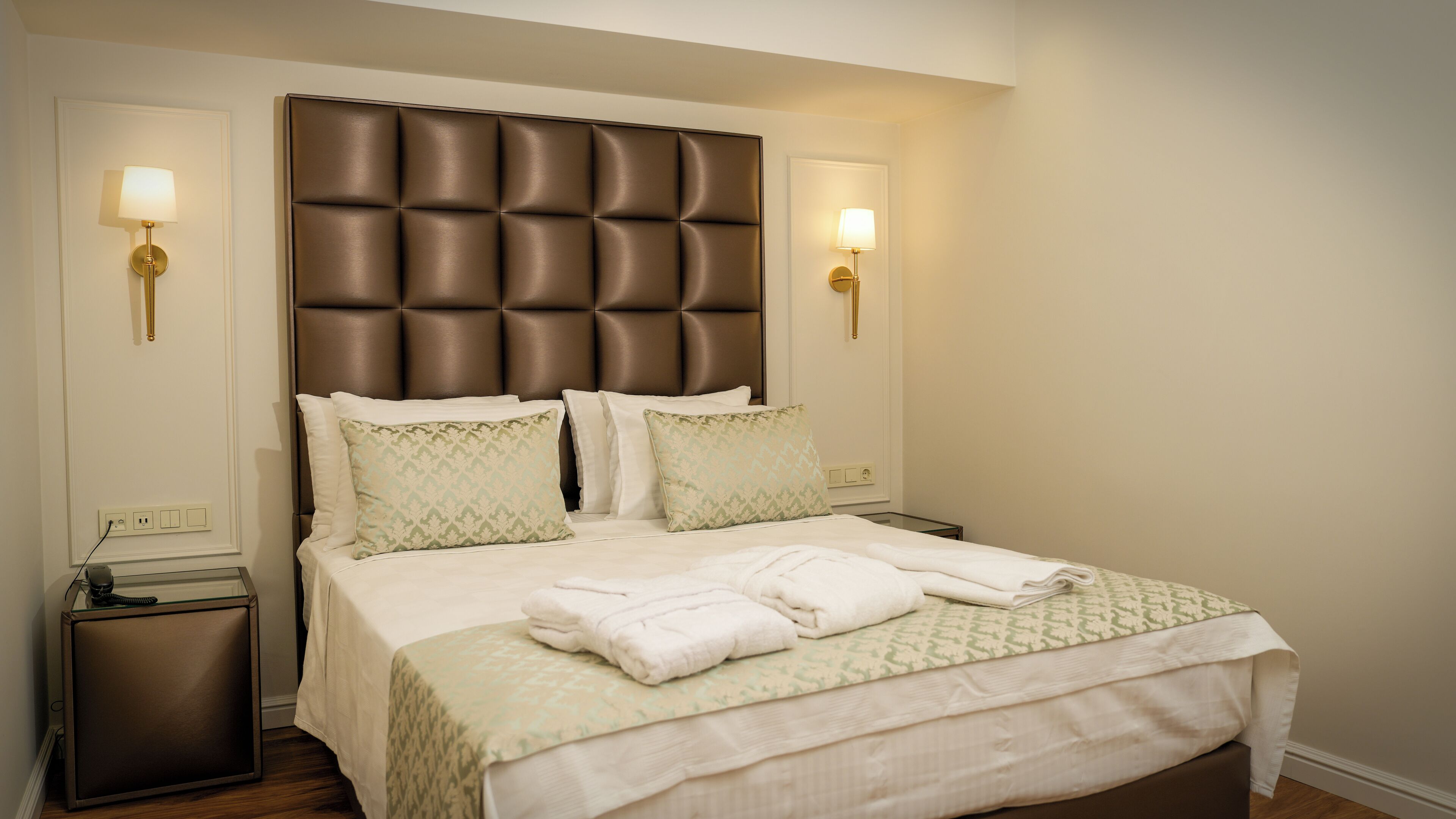 A neatly made bed with a tufted headboard, two bedside lamps, and a small bedside table with a telephone.