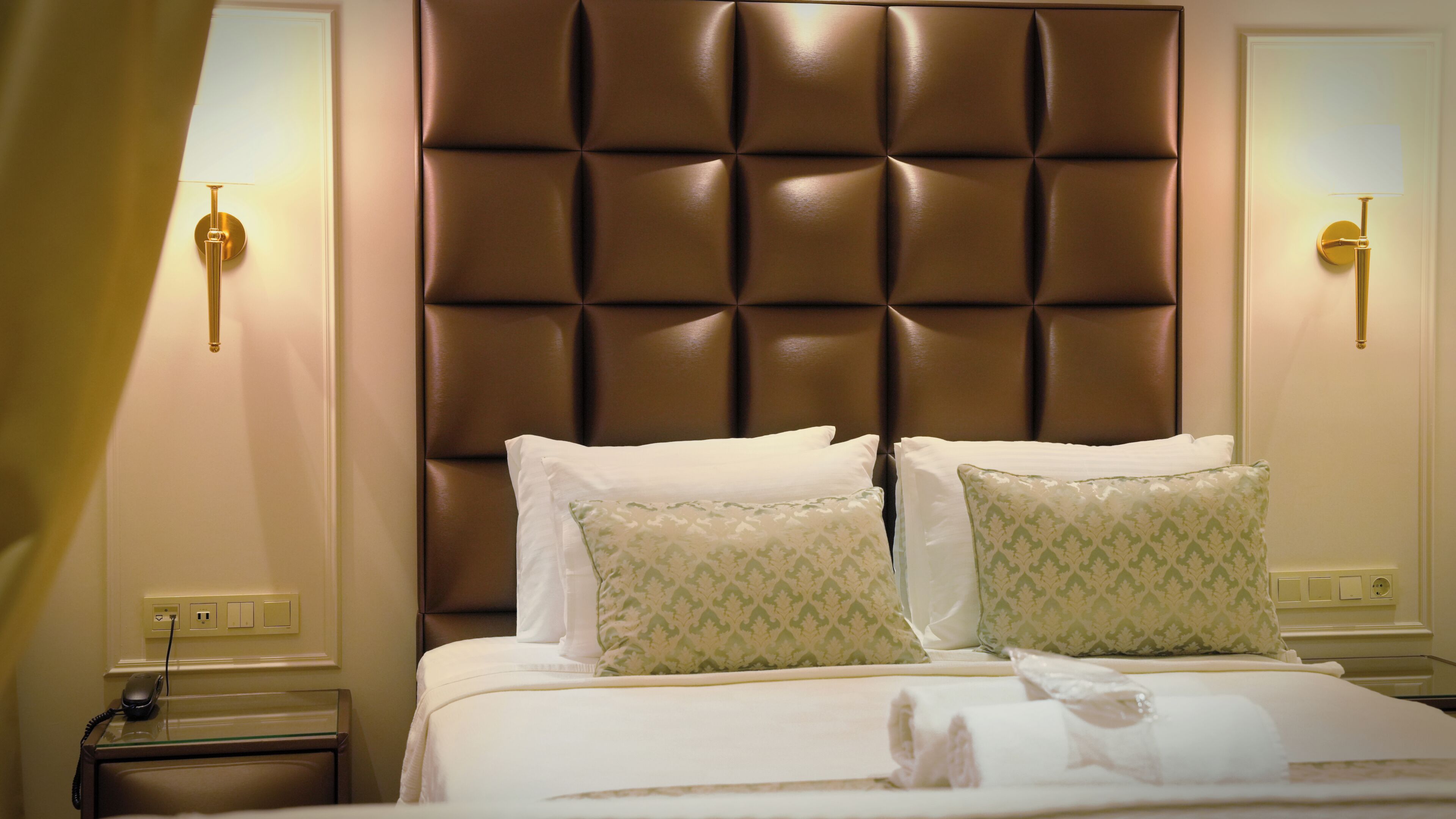 A hotel room with a tufted headboard, two bedside tables with lamps, and a bed with white linens and patterned pillows.