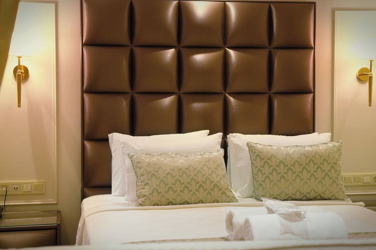 A hotel room with a tufted headboard, two bedside tables with lamps, and a bed with white linens and patterned pillows.