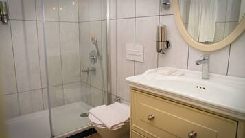 Un baño moderno con ducha envuelta en vidrio, un lavabo blanco sobre un mueble auxiliar color beige y un espejo sobre el lavabo.
