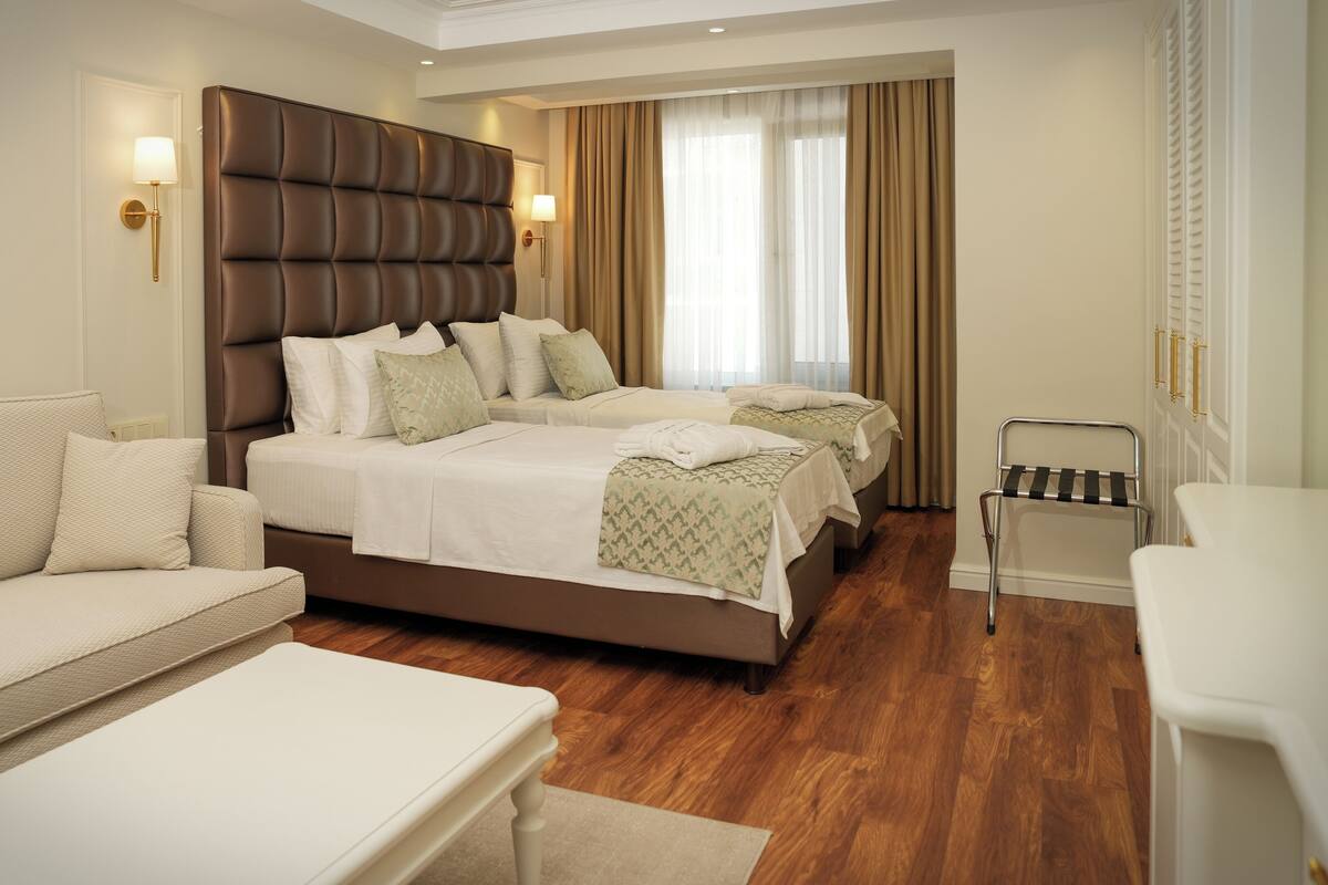 A hotel room with a large bed, a sofa, a chair, and a bedside table.