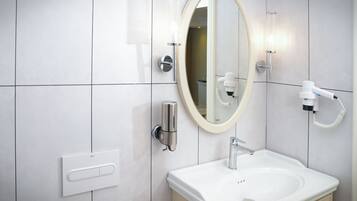 Un baño moderno con un lavamanos blanco, un espejo redondo, un cabezal de ducha manual y un dispensador de jabón de pared.
