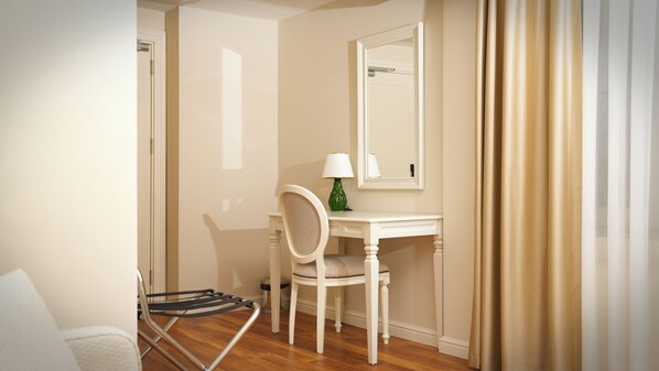 A small, neatly arranged room with a white desk, a chair, a mirror, and a lamp.