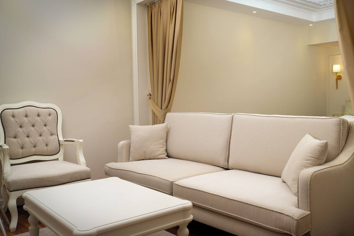 A room with a beige upholstered sofa, a matching ottoman, and a tufted armchair.