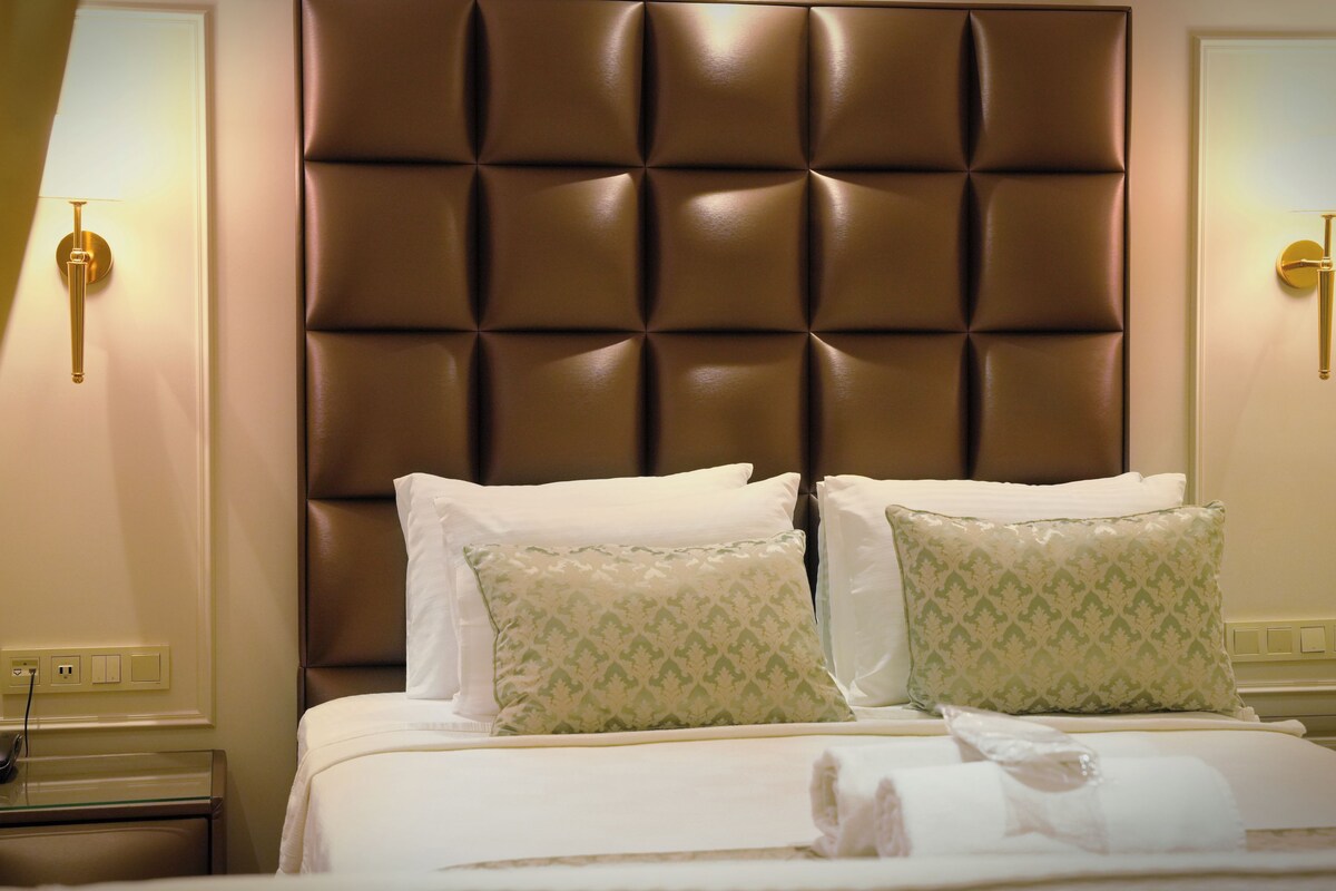 A hotel room with a tufted headboard, two bedside tables with lamps, and a bed with white linens and patterned pillows.
