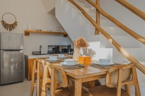 A modern kitchen with a stainless steel refrigerator, wooden dining table with chairs, and a staircase leading to an upper level. - Luana Villa by Betterplace (Canggu)