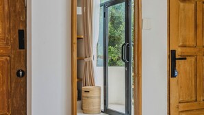 Un pasillo con una puerta de madera a la izquierda, un ventanal con marco de madera y cortinas, y una cesta en el suelo.