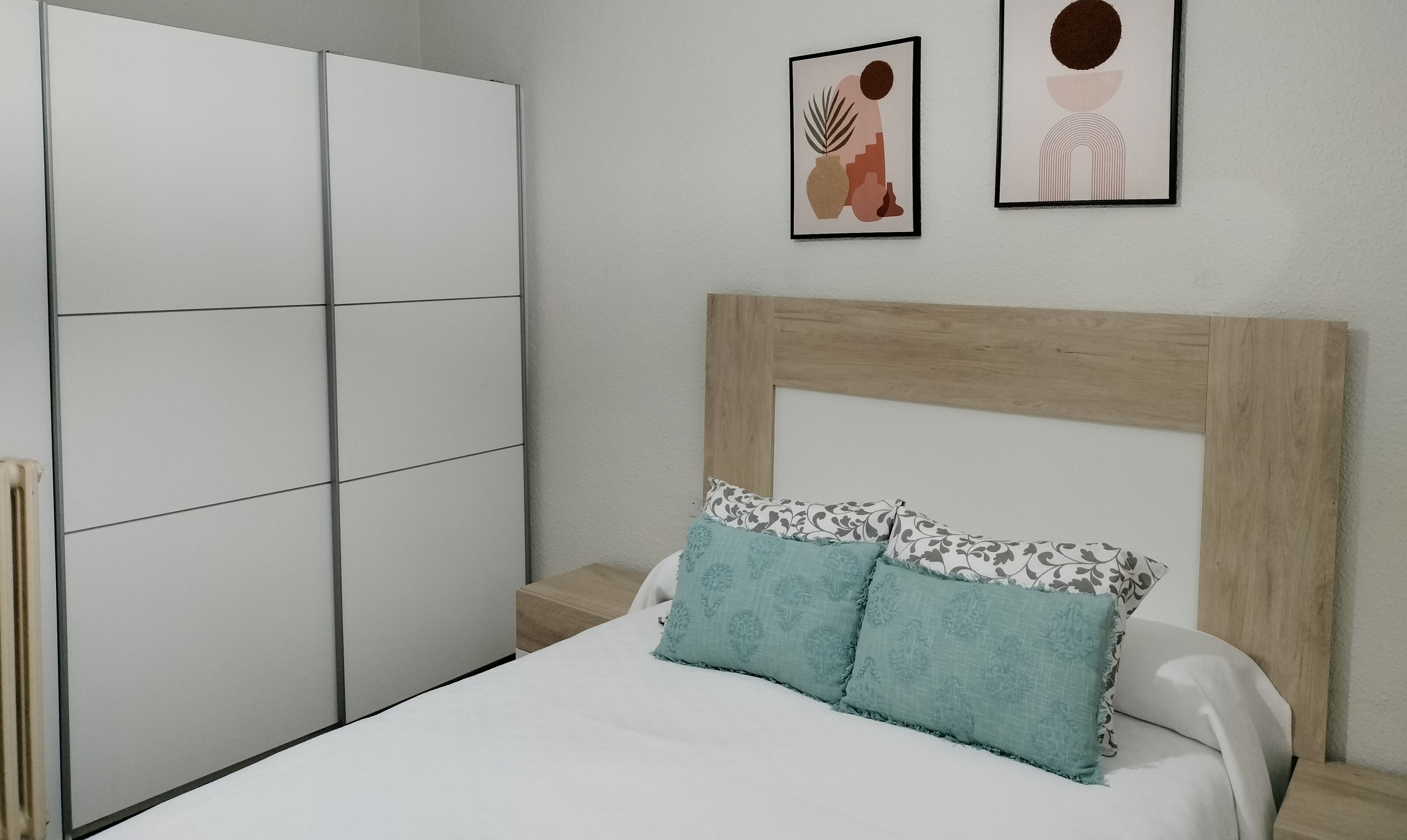 Un dormitorio con cama, armario y dos cuadros en la pared.