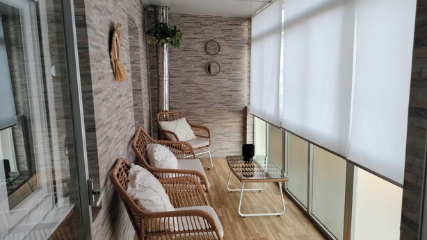 A balcony with wicker chairs, a glass table, and a view of the city.
