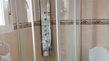 Douchecabine met glazen deur, toilet en wastafel.