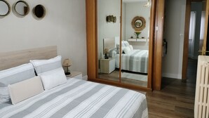 A bedroom with a large bed, a nightstand, a mirror, and a wooden floor.
