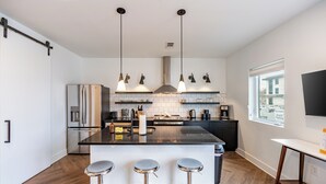 Una cocina moderna con una isla central, electrodomésticos de acero inoxidable, iluminación colgante y vistas al exterior.
