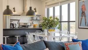 Una cocina moderna con lámparas colgantes, una zona de comedor con sillas transparentes y un ventanal grande.