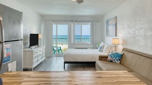 Ein Schlafzimmer mit Bett, Schminktisch, Fernseher, Deckenventilator und Meerblick durch große Fenster.