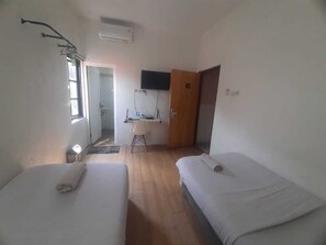 Ein Zimmer mit zwei Betten, einem Schreibtisch, einem Fernseher und einer Tür.