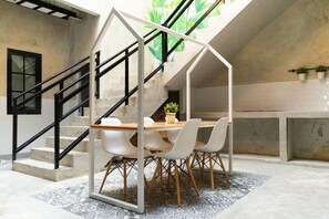 A modern interior with a dining area featuring a table and chairs, a staircase with a black railing, and a concrete wall with potted plants. - Fybed Guesthouse (Semarang)