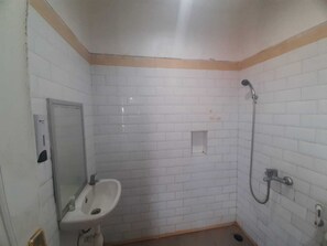 Ein kleines Badezimmer mit weißen Fliesen, einem Waschbecken, einem Spiegel und einer Dusche.