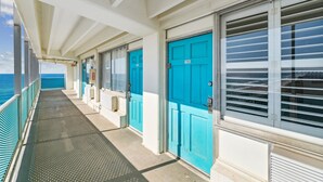 A corridor with blue doors and windows, leading to a balcony with a view of the ocean. - Fontainebleau 706 by AvantStay | Beachfront+Views (Panama City Beach)