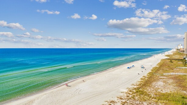 A beach with clear turquoise water, a sandy shore, and a few buildings in the background. - Fontainebleau 706 by AvantStay | Beachfront+Views (Panama City Beach)