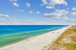 En strand med kristallklart turkost vatten, en sandstrand och några byggnader i bakgrunden.
