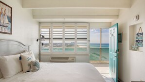 A bedroom with a bed, a window with blinds, a view of the sea, and a teal door. - Fontainebleau 706 by AvantStay | Beachfront+Views (Panama City Beach)