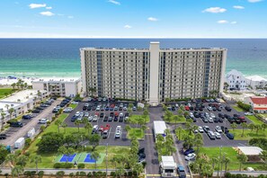 A high-rise hotel with a parking lot, a tennis court, and a view of the ocean.
