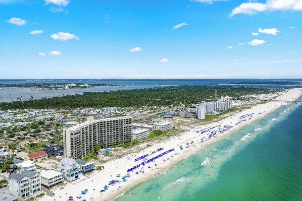 A coastal hotel with multiple buildings, a beach with umbrellas, and a view of the ocean.