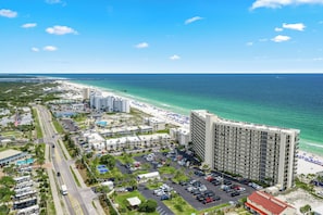 A high-rise hotel with a parking lot, beach, and ocean view.