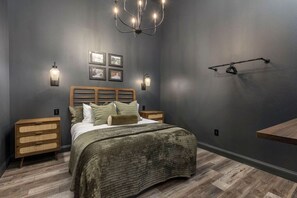 A bedroom with a bed, bedside tables, wall-mounted light fixtures, and a hanging light fixture. - The Downtown Derby Stay (Louisville)