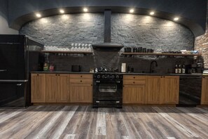 A kitchen with a stone wall, wooden cabinets, a black refrigerator, and an oven. - The Downtown Derby Stay (Louisville)