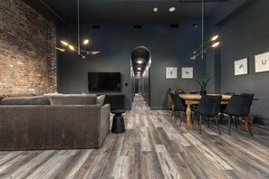 Ein modernes Interieur mit Backsteinwand, einer Couch, einem Esstisch mit Stühlen und einem an der Wand befestigten Fernseher.