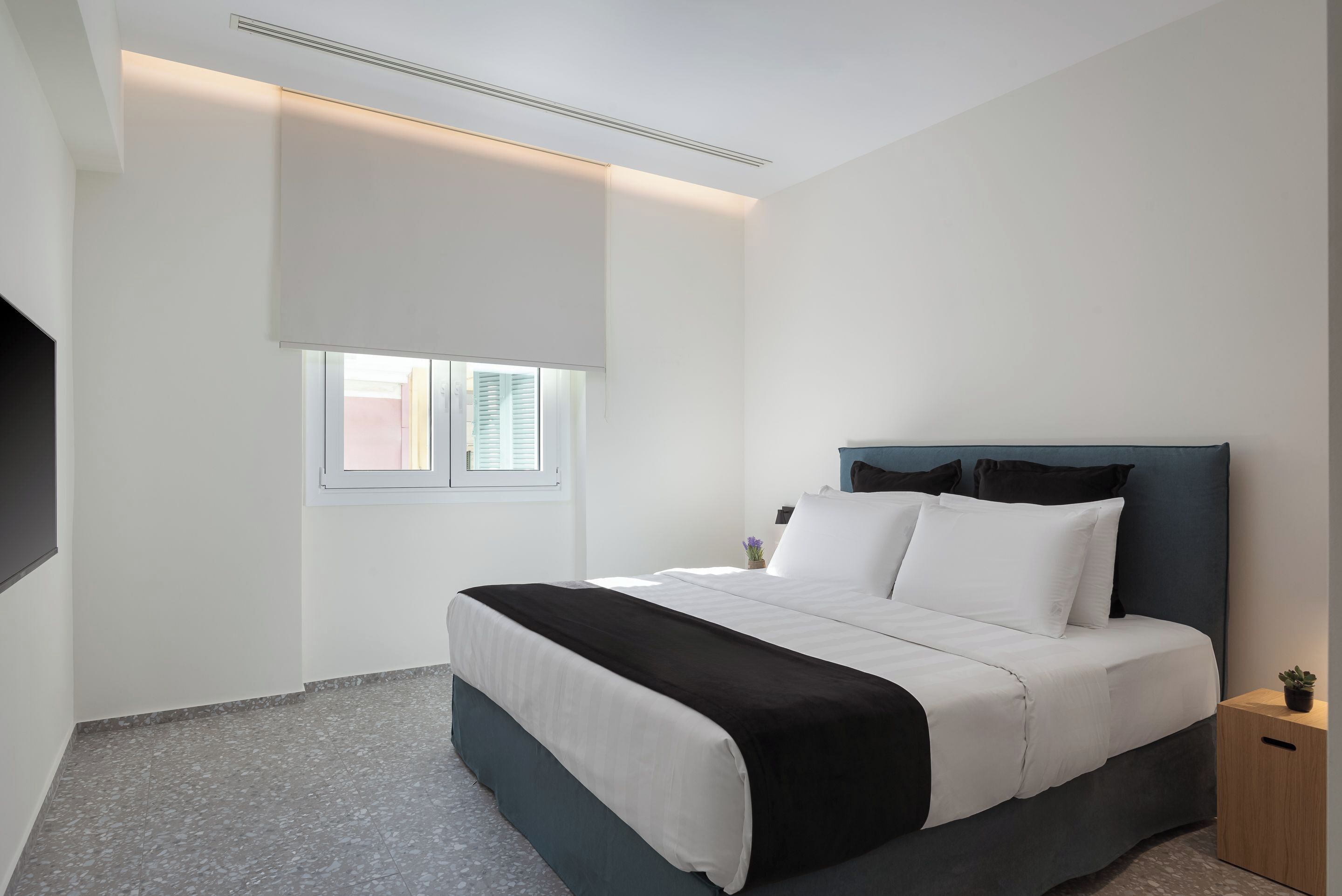A modern bedroom with a bed, bedside table, and a window with blinds.
