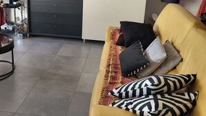 Uma sala de estar com um sofá amarelo, uma TV de tela plana, um armário branco e um quadro na parede.