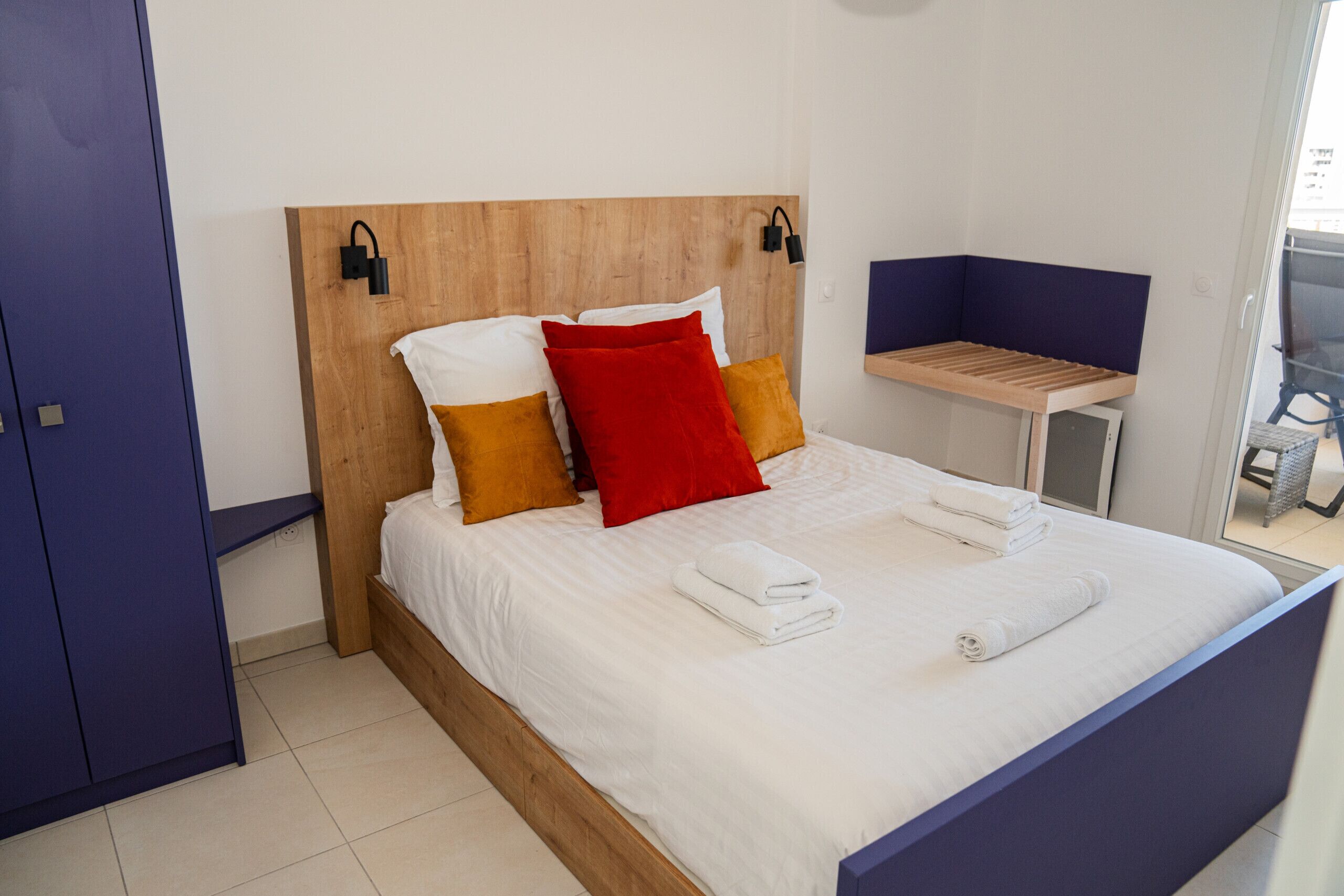 A neatly made bed with white linens and a few pillows, a wooden headboard, and a small table beside the bed.